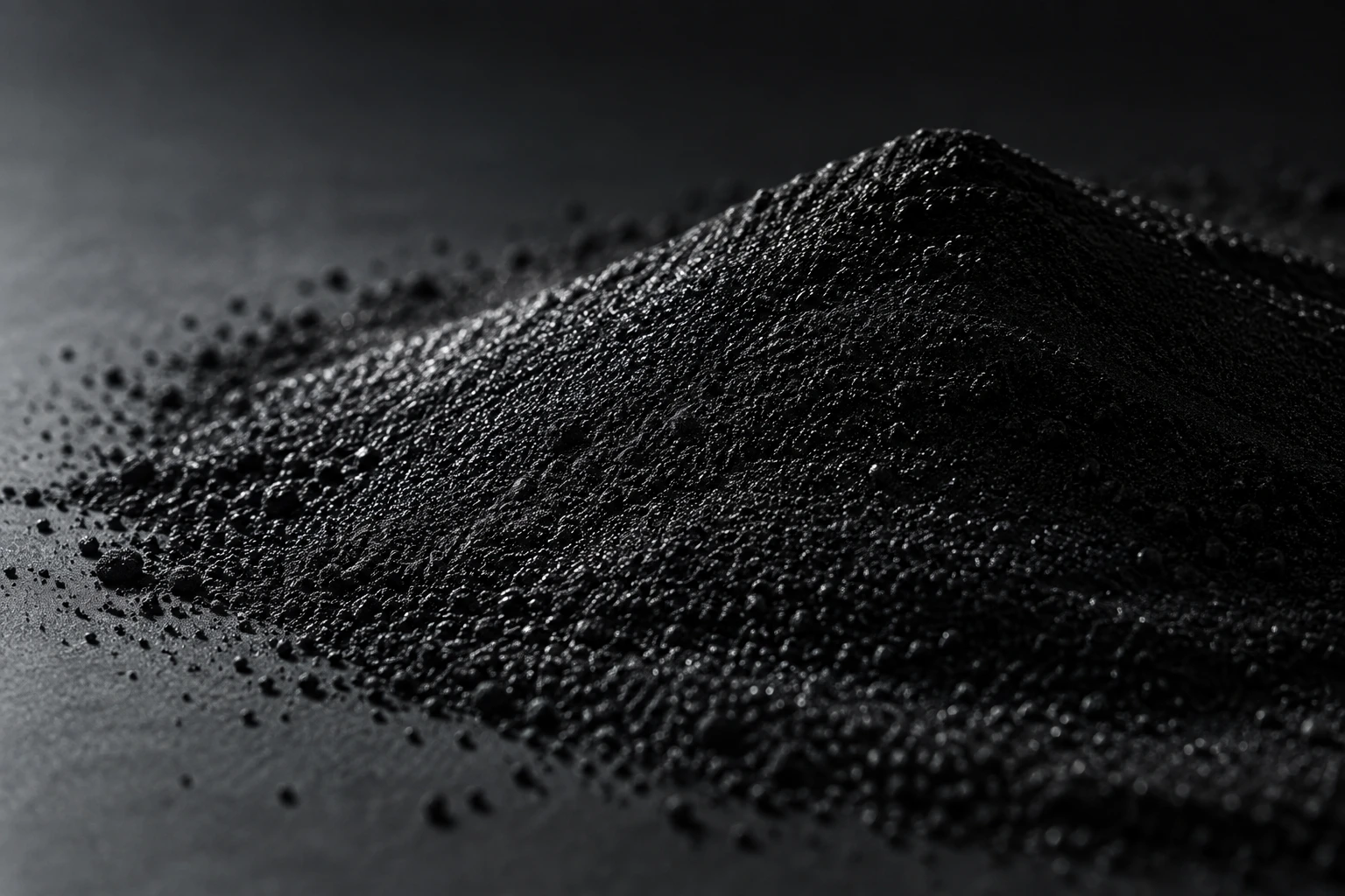 Conceptual black powder dune with silvery side lighting on a charcoal surface